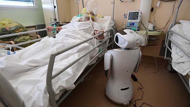 يقف أحد الروبوتات الستة في مستشفى "سيركولو دي فاريزي" بالقرب من مريض بفيروس كورونا